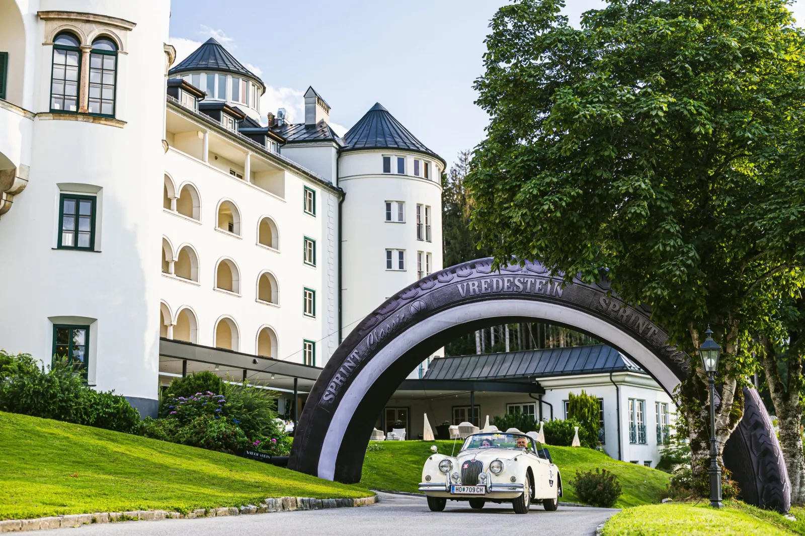 A classic white convertible drives beneath a large tyre-shaped Vredestein Sprint Classic arch at the Ennstal-Classic rally. (Photo: Apollo Tyres)