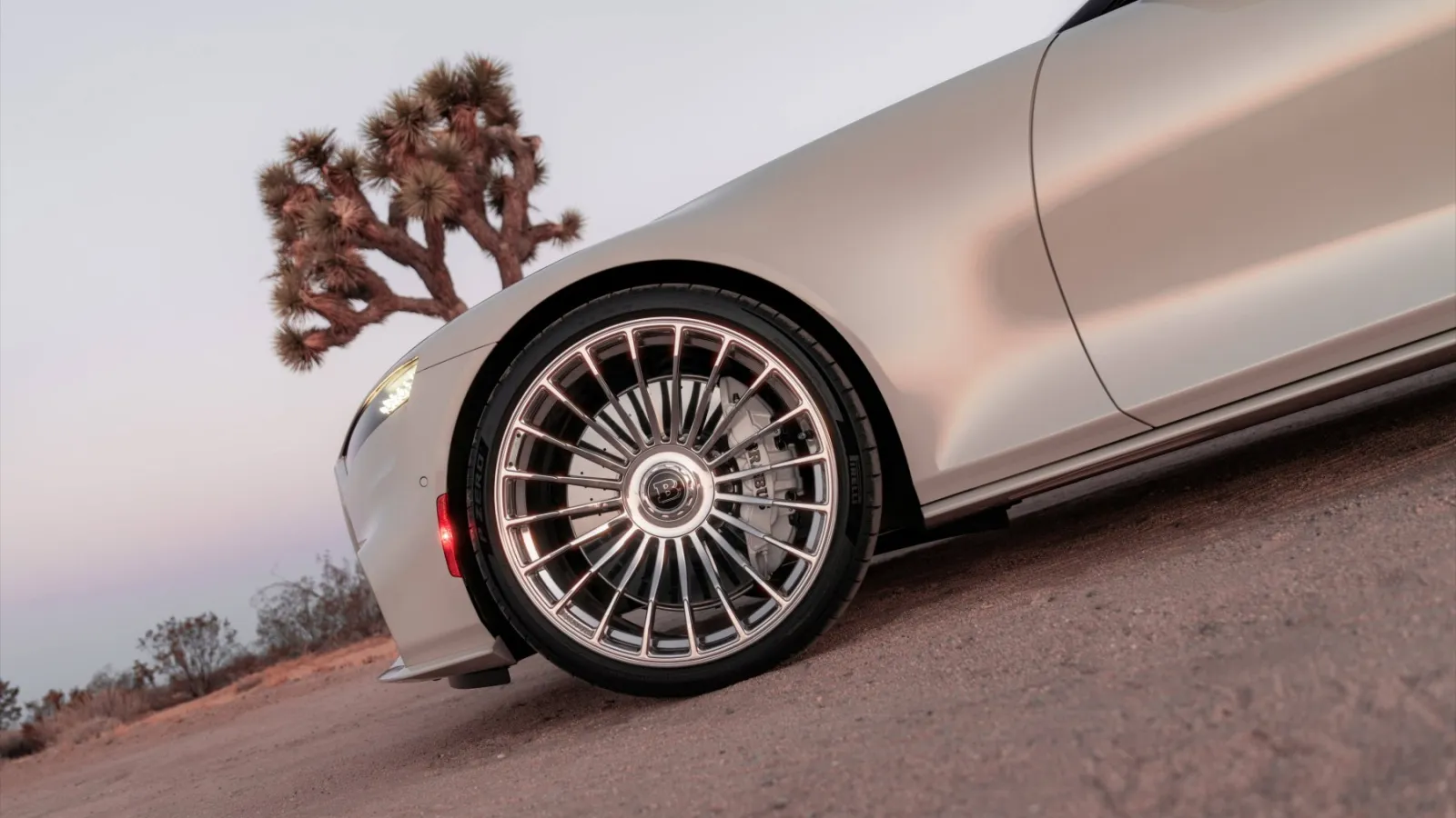 Low-angle side shot of a champagne-gold Brabus supercar wheel featuring a 22-inch Pirelli P Zero tyre and multi-spoke chrome rim in front of a Joshua tree desert landscape.