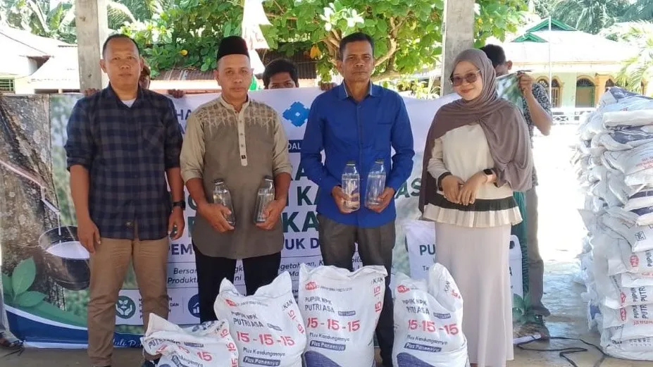 Project representatives standing with smallholder farmers behind sacks of fertilizer and liquid farm inputs in front of an event banner in Sumatra.